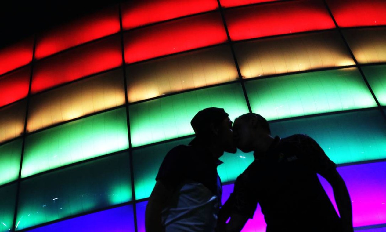 Casal homoafetivo se beija diante da Movistar Arena colorida com a bandeira do arco-íris durante o Dia Internacional do Orgulho LGBTQIA+, em Bogotá, Colômbia Foto: DANIEL MUNOZ / AFP