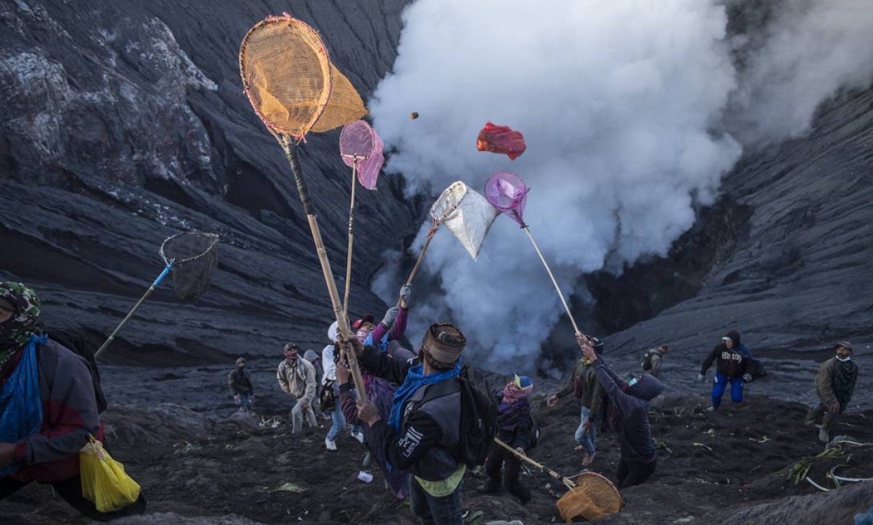 Pessoas tentam pegar oferendas lançadas por membros da tribo Tengger no cume do vulcão ativo Monte Bromo, em Probolinggo, província de Java Oriental Foto: JUNI KRISWANTO / AFP