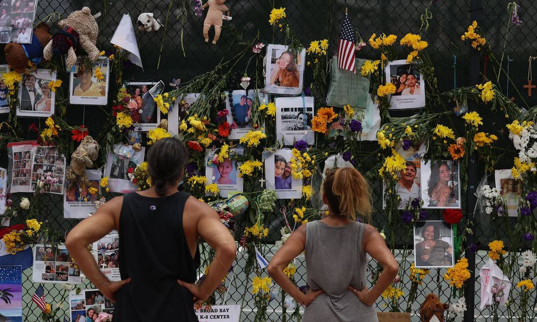 Pessoas olham o memorial com fotos de alguns dos desaparecidos após o desabamento, em 24 de junho, de um prédio em Surfside, na Flórida. Quase duas semanas depois, autoridades afirmaram que não há mais sobreviventes Foto: Joe Raedle / AFP