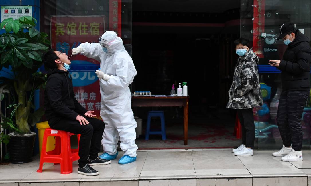 Foto tirada em março de 2020 mostra pessoas esperando na fila enquanto um profissional de saúde coleta uma amostra de esfregaço de uma pessoa para ser testada para o novo coronavírus em Wuhan, na região central da China Foto: HECTOR RETAMAL / AFP
