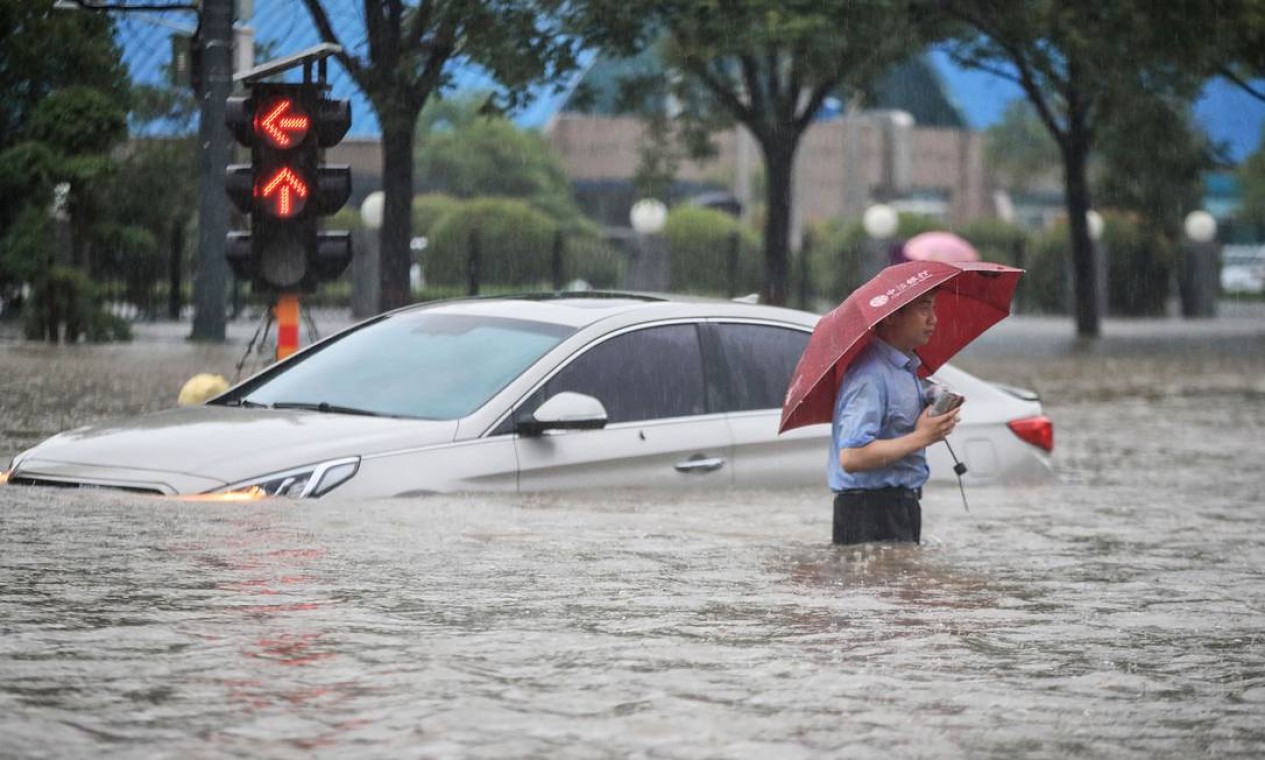 Homem passa por um carro submerso ao longo de uma rua inundada após fortes chuvas em Zhengzhou, na província central de Henan, na China Foto: STR / AFP