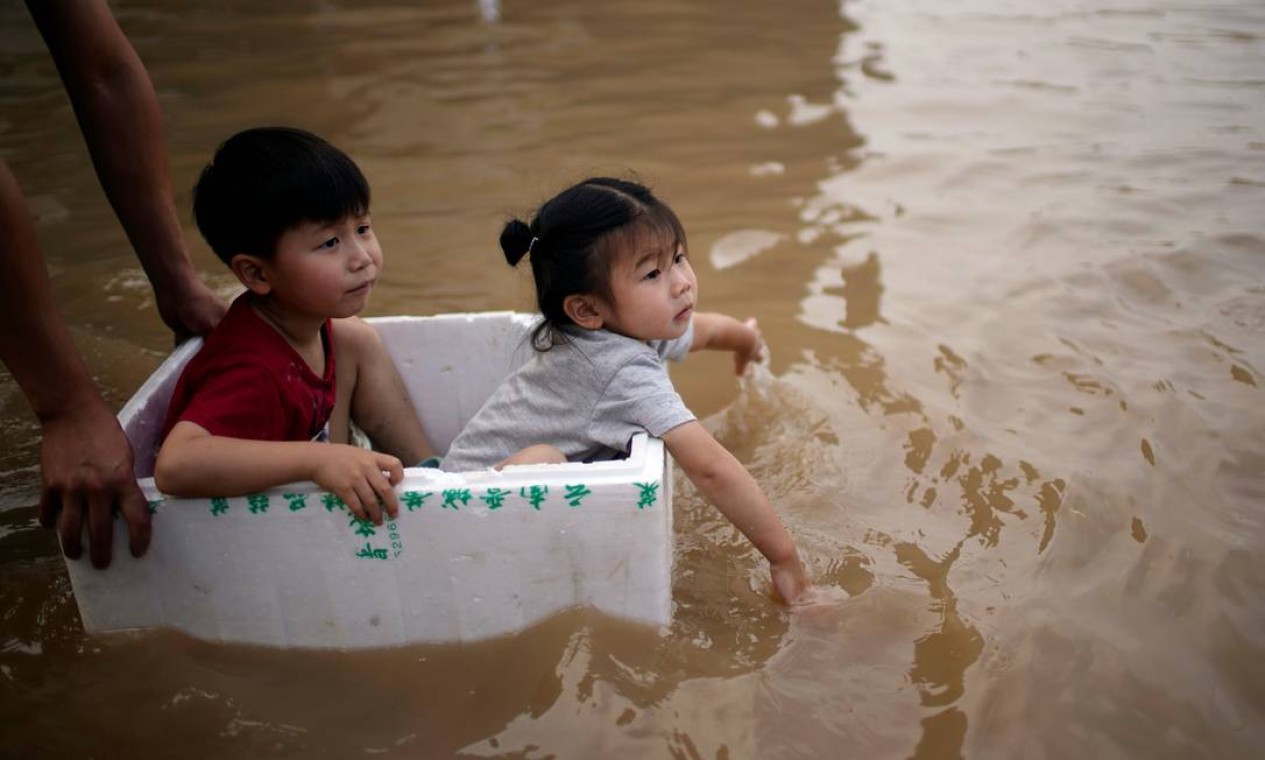 Crianaçs são levadas em caixa de isopor por rua inundada em Zhengzhou Foto: ALY SONG / REUTERS