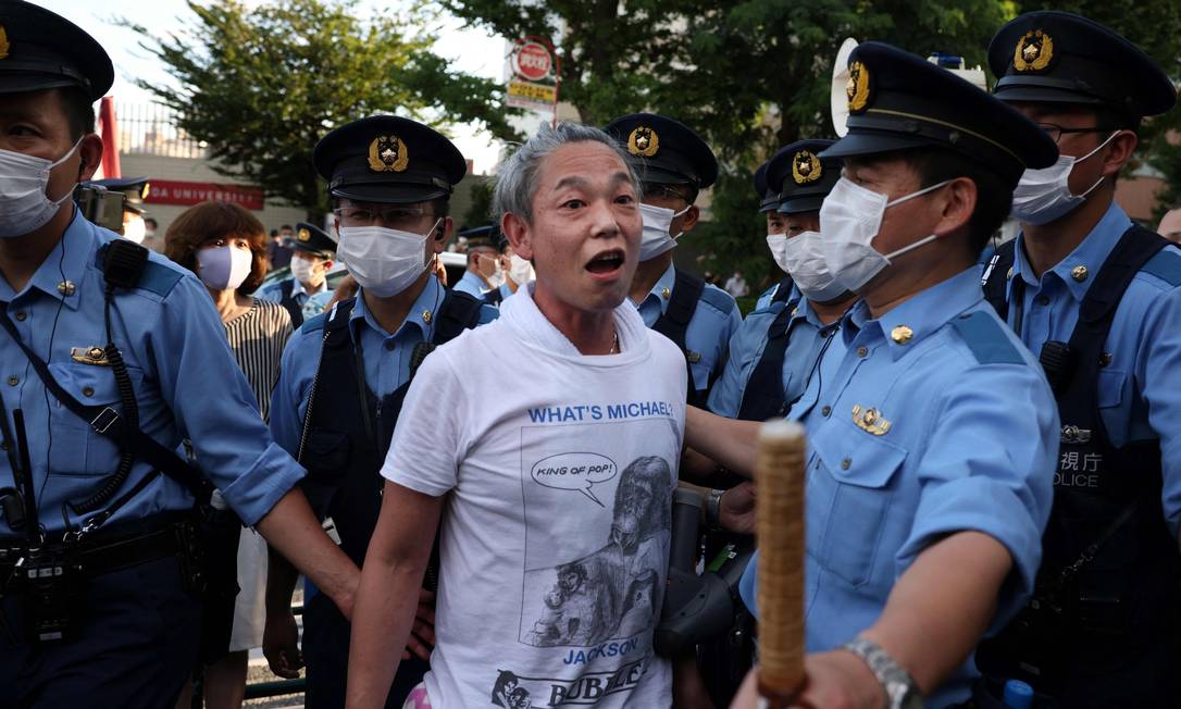 Policiais escoltam um manifestante que protestava contra os Jogos Olímpicos de Tóquio em 2020 depois de confusão com fãs das olimpíadas Foto: YUKI IWAMURA / AFP