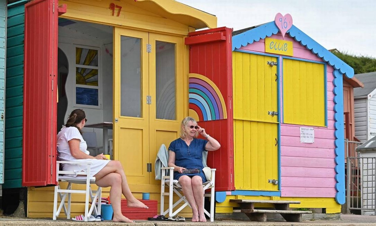 Banhistas conversam em frente a cabanas de cores vivas em frente à praia de Walton-on-the-Naze Foto: JUSTIN TALLIS / AFP