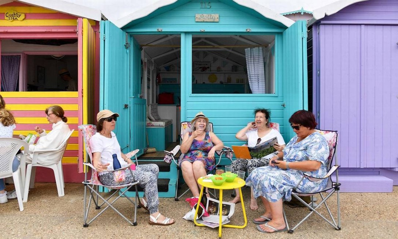 Banhistas conversam em frente a cabanas de praia na orla de Walton-on-the-Naze: essas casinhas de madeira, tão tradicionais no litoral britânico, ficaram ainda mais populares na pandemia Foto: JUSTIN TALLIS / AFP