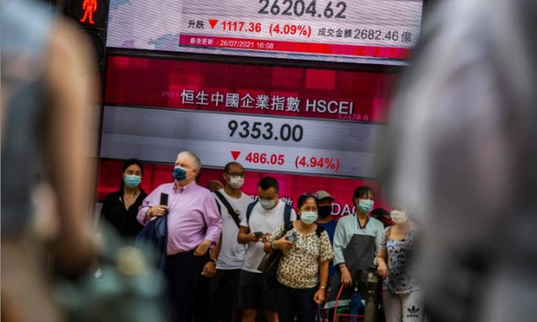Pessoas paradas em frente a um painel eletrônico que mostra o Índice Hang Seng, da bolsa de Hong Kong, depois que as ações despencaram após decisão da China de intervir das instituições de ensino privado Foto: AFP