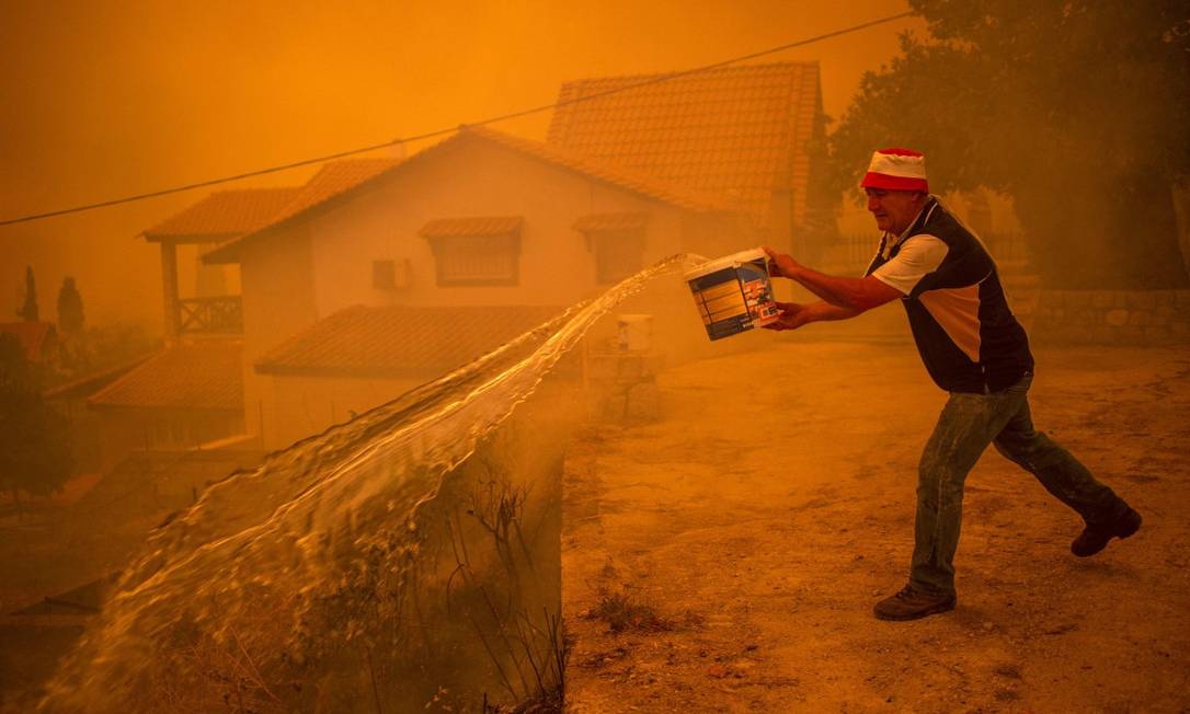 A resident tries to put out fires with a bucket during a fire on the island of Euboea Photo: ANGELOS TZORTZINIS / AFP