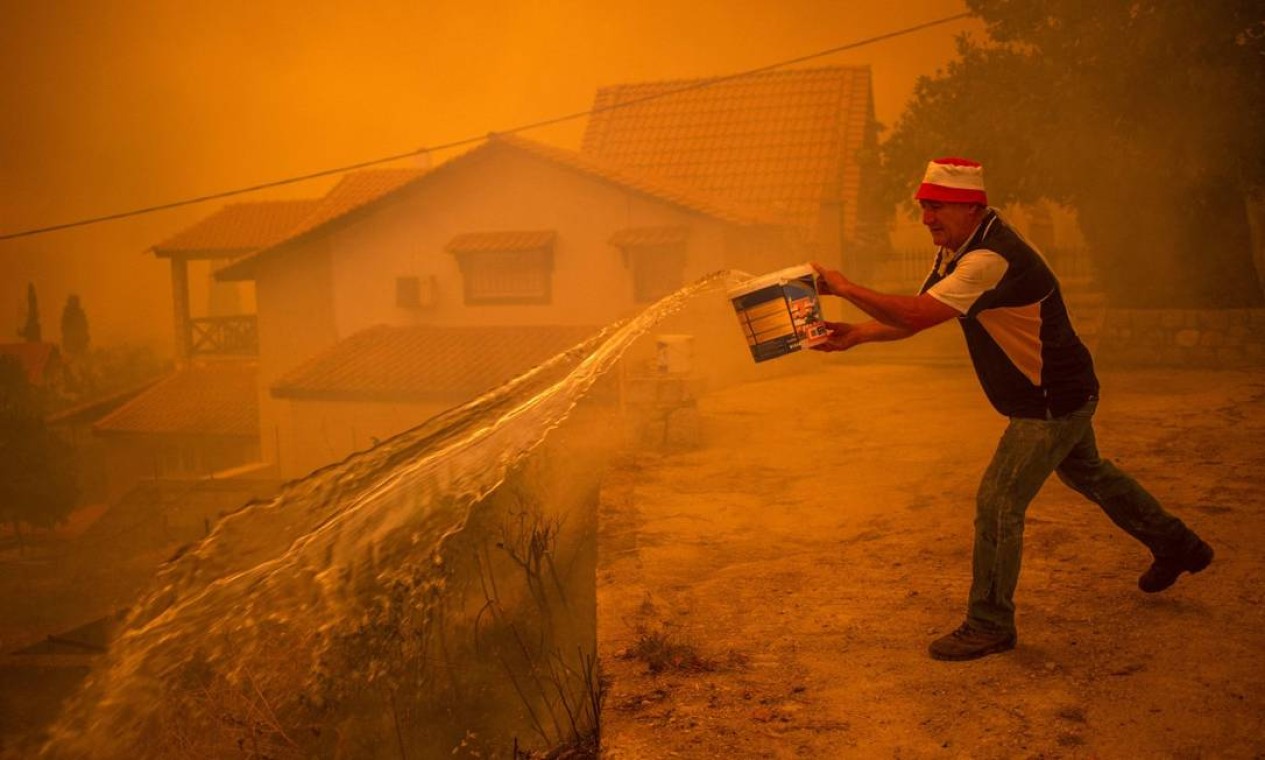 Morador tenta apagar chamas com balde durante incêndio na ilha de Eubeia Foto: ANGELOS TZORTZINIS / AFP
