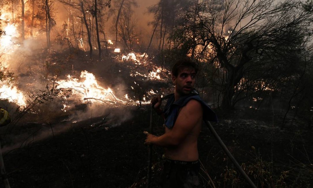 Com mangueira, morador tenta conter chamas durante incêndio na Ilha de Ilha de Eubeia, na Grécia Foto: ALEXANDROS AVRAMIDIS / REUTERS