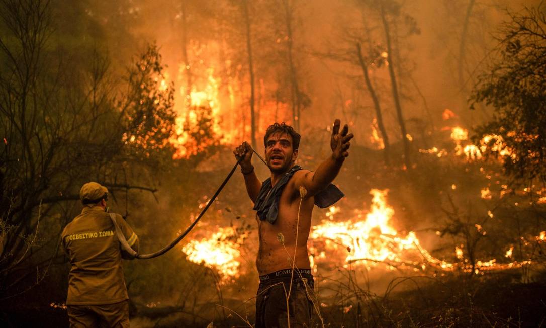 Homem segura mangueira em tentativa de apagar o incêndio na ilha grega de Evia, a segunda maior do país Foto: ANGELOS TZORTZINIS / AFP/8-8-21