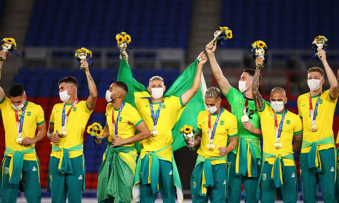 Jogadores da seleção brasileira no pódio com os agasalhos oficiais da delegação amarrados na cintura Foto: THOMAS PETER / REUTERS