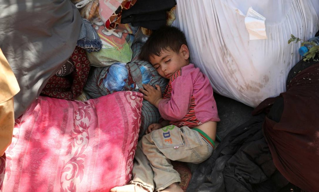 Uma criança dorme entre trouxas de roupa em um parque que está sendo usado como abrigo em Cabul Foto: REUTERS