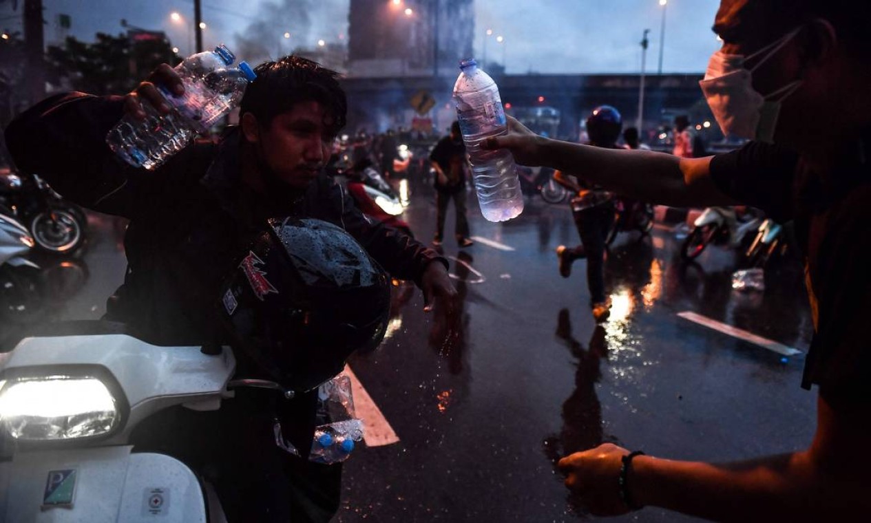 Um manifestante pró-democracia derrama água nos olhos de outro para ajudar com gás lacrimogêneo enquanto entram em confronto com a polícia durante um protesto pedindo a renúncia do primeiro-ministro Prayut Chan-O-Cha Foto: LILLIAN SUWANRUMPHA / AFP
