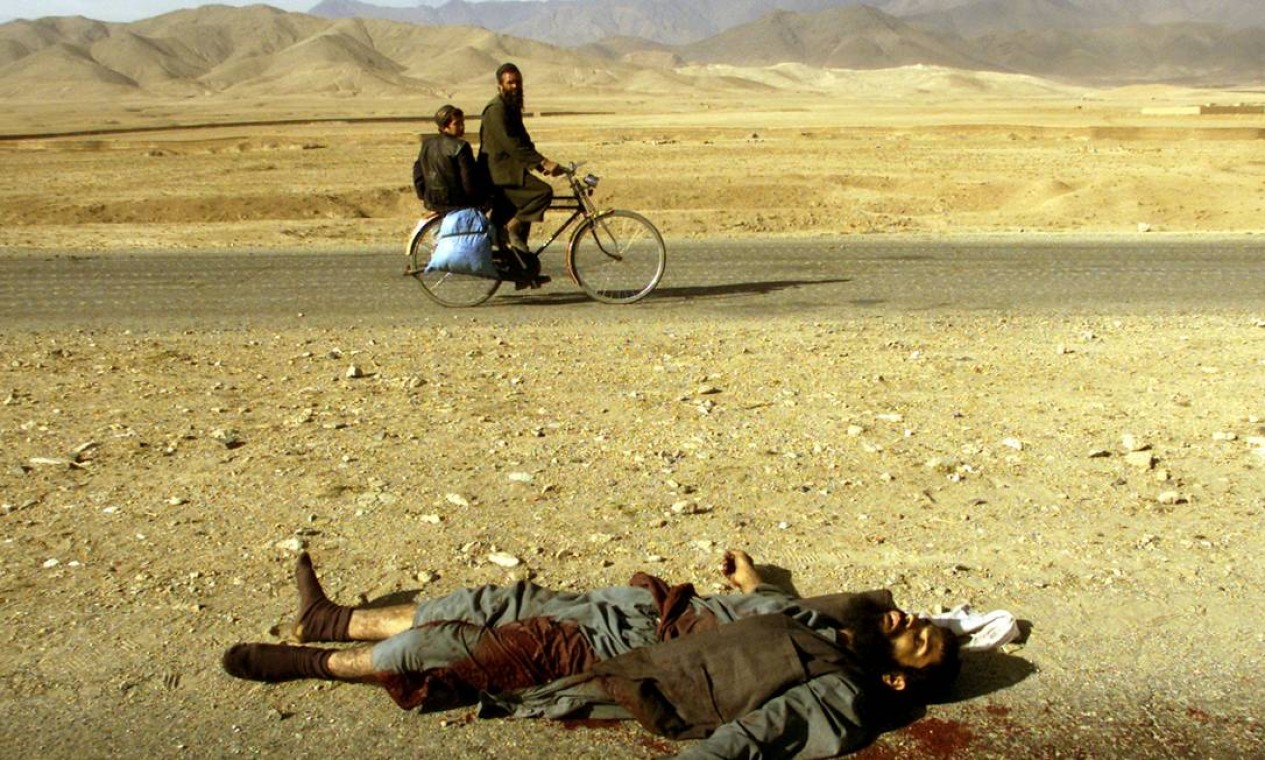 Afegão e filho passam de bicicleta pelo corpo de um talibã morto durante confronto no norte de Cabul Foto: YANNIS BEHRAKIS / REUTERS - 13/11/2001