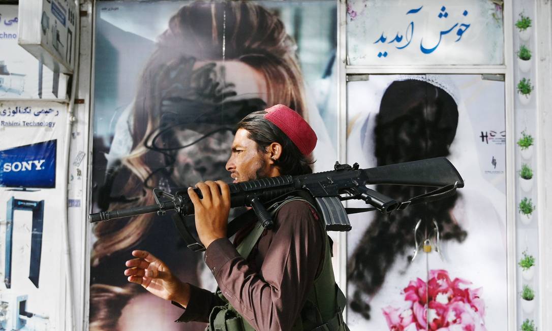 Combatente do Talibã passa diante de cartaz com imagens de mulheres cobertas por tinta spray no distrito de Shahr-é Naw, em Cabul Foto: WAKIL KOHSAR / AFP