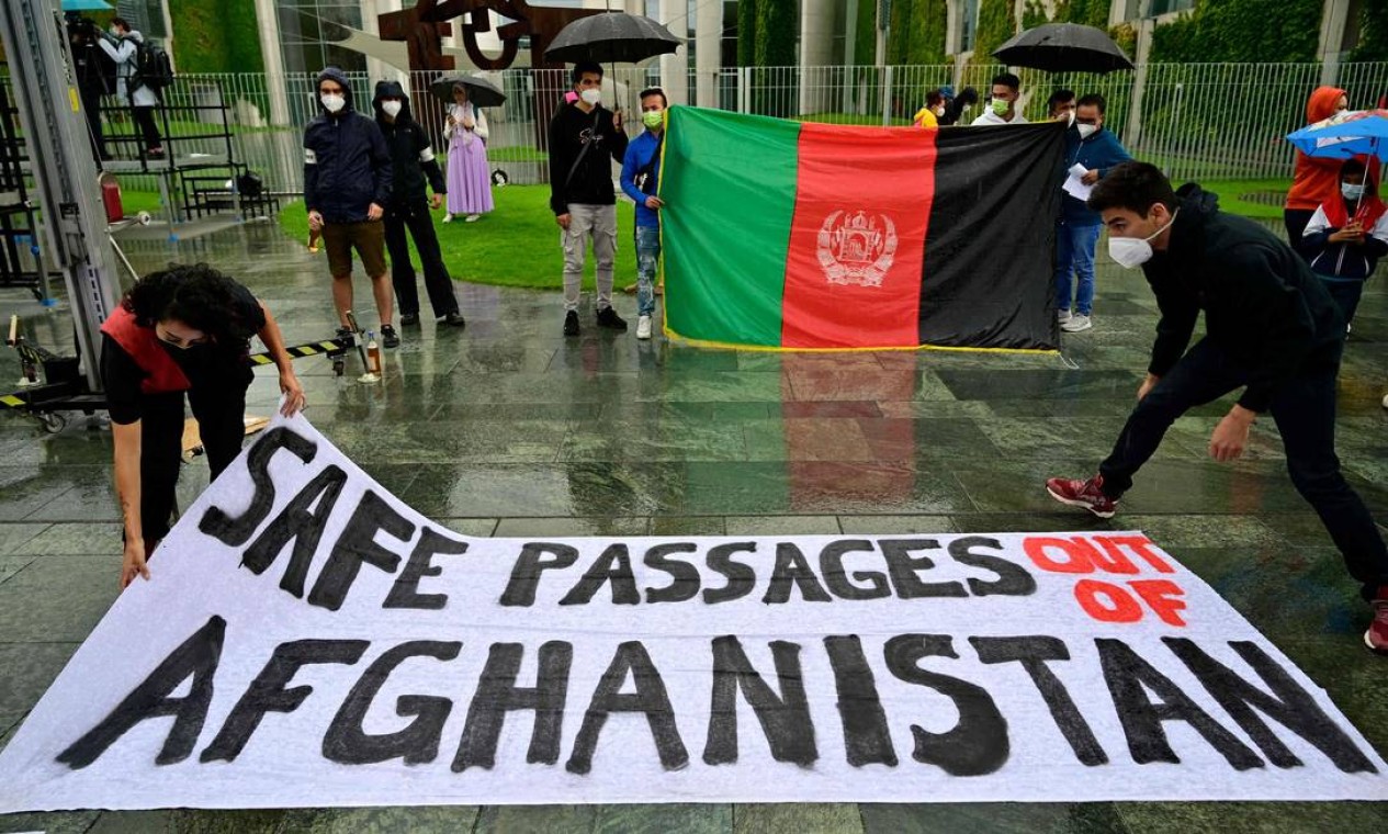 Manifestantes exibem uma bandeira do Afeganistão e seguram uma faixa com a frase "passagens seguras para fora do Afeganistão", em Berlim Foto: JOHN MACDOUGALL / AFP