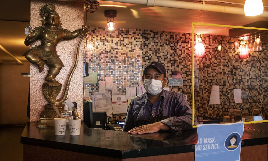 Funcionário de um restaurante no Queens ao lado de uma barreira de plástico anti-covid. Foto: Kirsten Luce/The New York Times / NYT