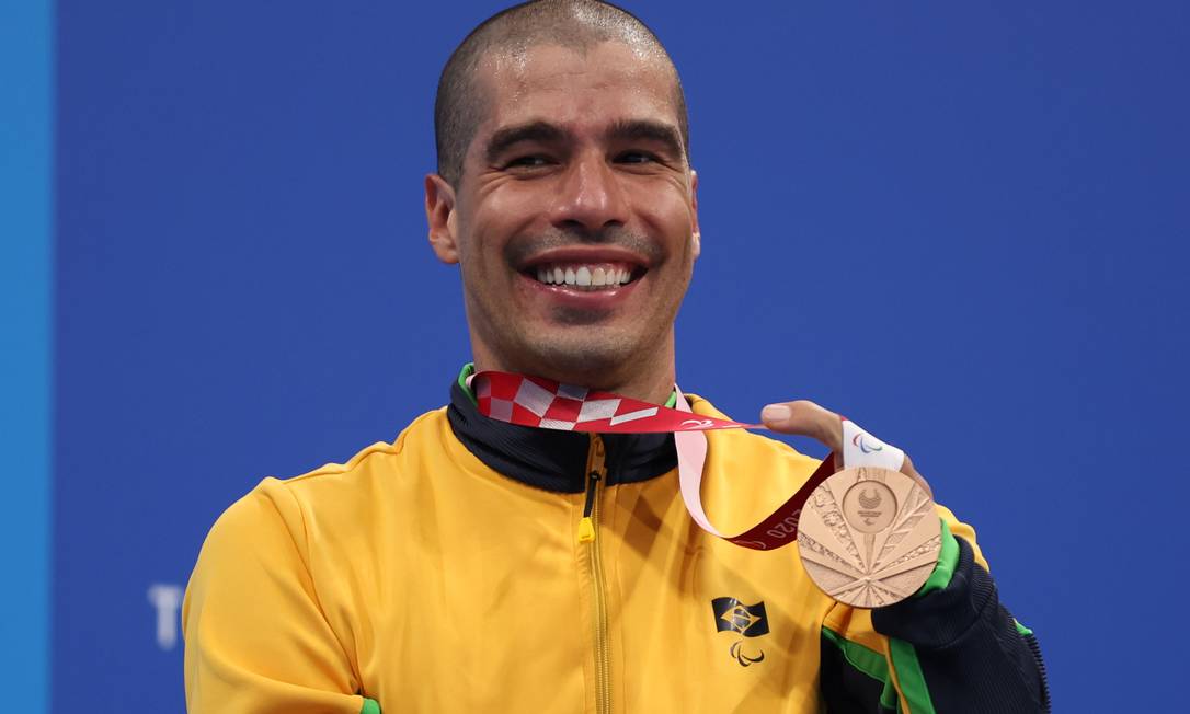 Atleta Daniel Dias, vestindo uniforme da delegação brasileira, posa com sua medalha de bronze, sorrindo no pódio de Tóquio. 