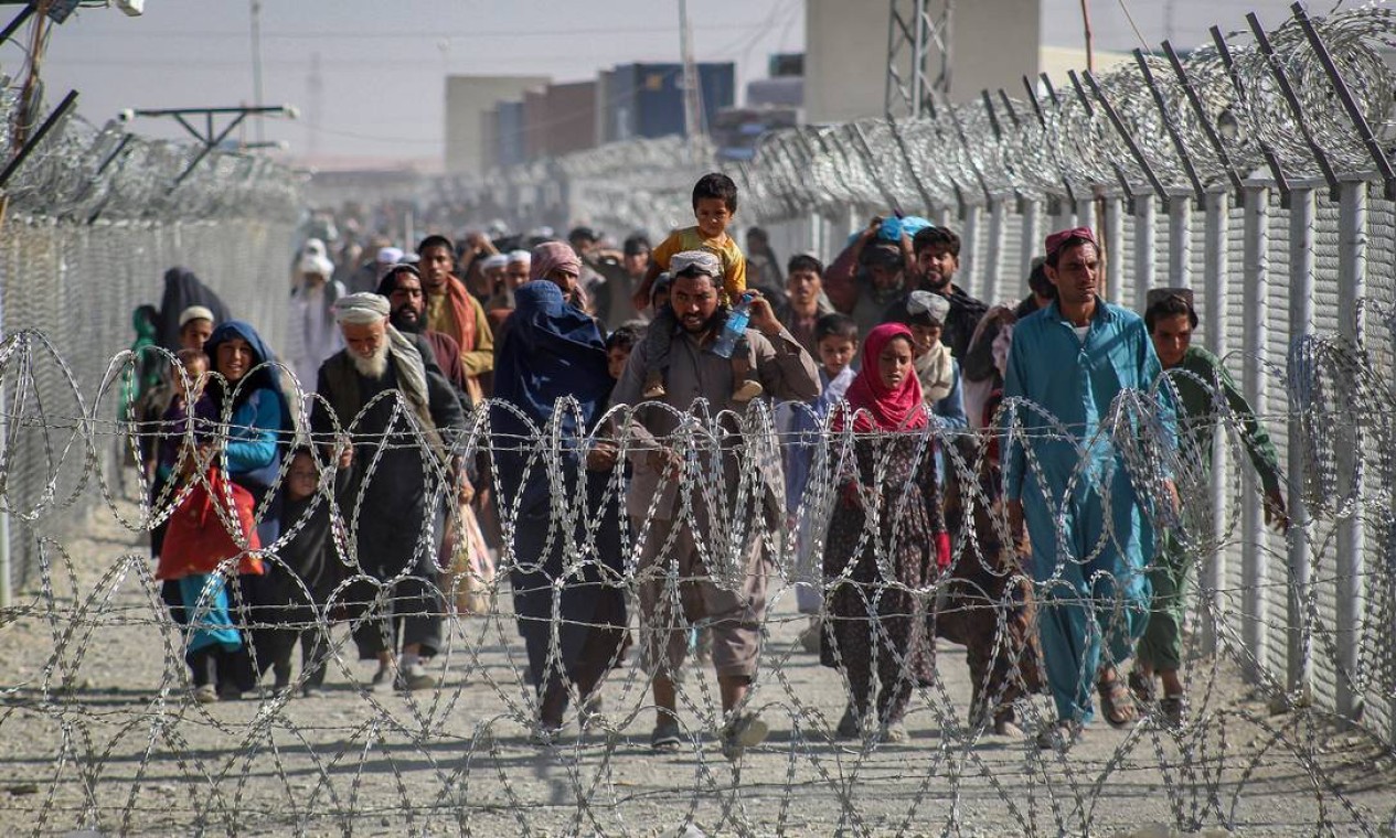 Afegãos caminham ao longo de cercas ao chegarem ao Paquistão através da fronteira entre os dois países, em Chaman, após a tomada militar do Talibã no Afeganistão Foto: - / AFP