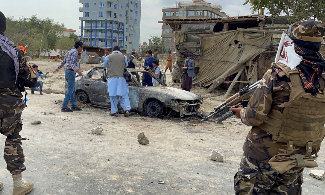 Sob o olhar de tropas do Talibã, moradores se aproximam de veículo atingido por míssel em Cabul, no Afeganistão Foto: STRINGER / REUTERS