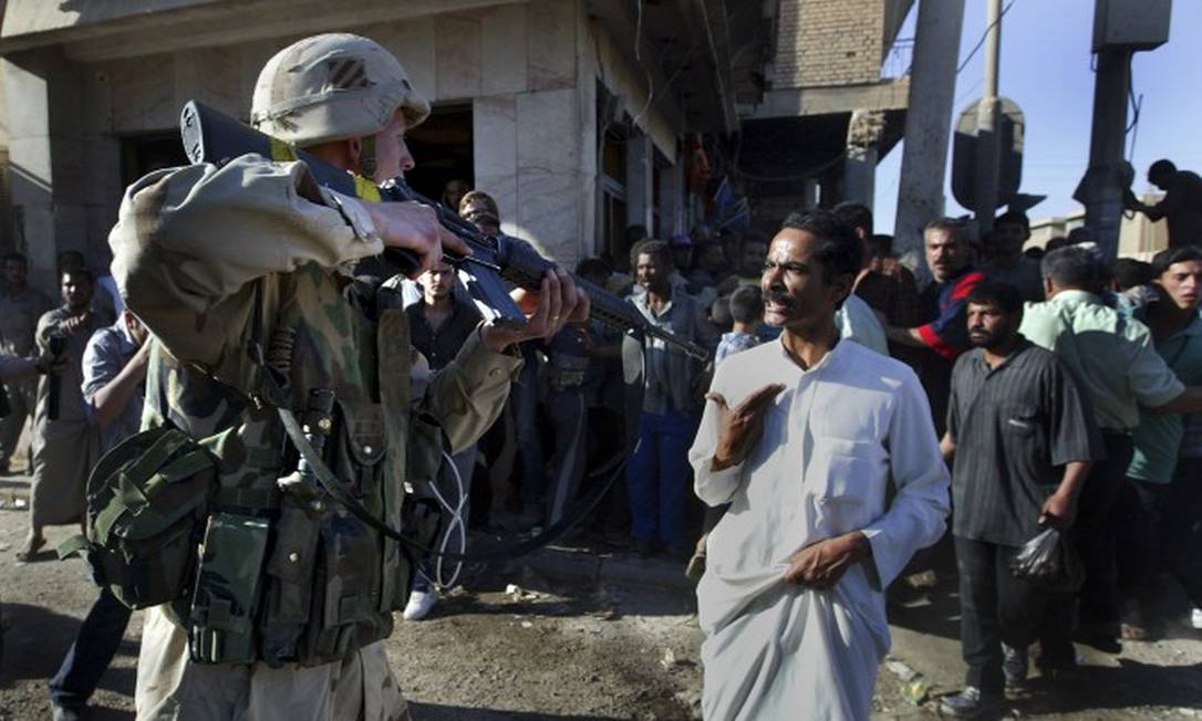 Dois meses após invasão do Iraque, soldado americano usa arma para mandar que civis se afastem de local de explosão em Bagdá Foto: TYLER HICKS / NYT/1-5-2003