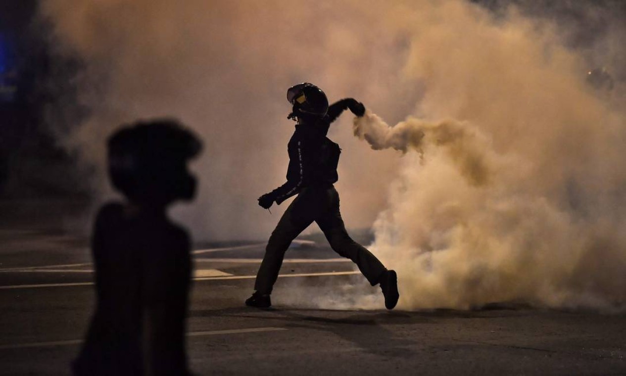 Manifestante joga para trás uma bomba de gás lacrimogêneo durante protestos contra o golpe militar na Tailândia Foto: LILLIAN SUWANRUMPHA / AFP