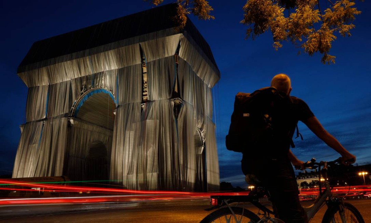 Ciclista olha para o Arco do Triunfo, em Paris, envolto em tecido prata-azul desenhado pelo saudoso artista Christo Foto: GEOFFROY VAN DER HASSELT / AFP