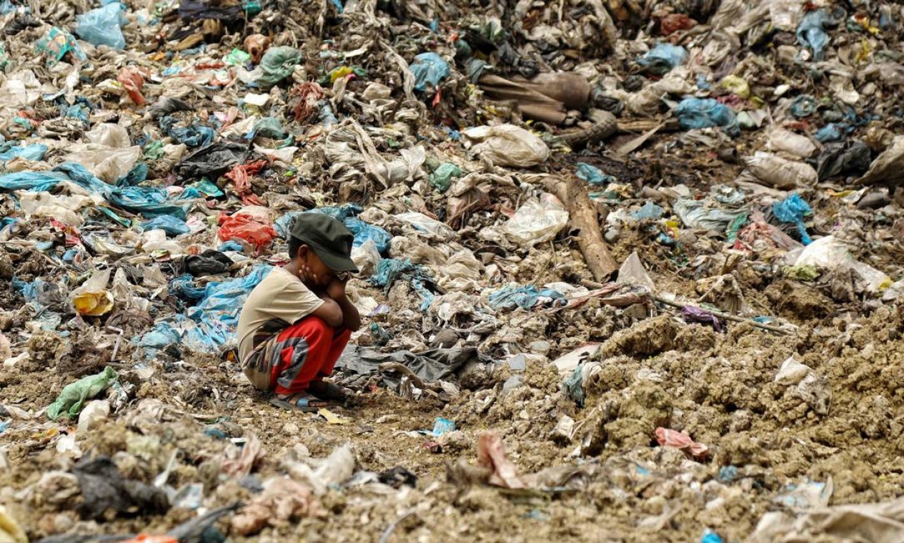 Filho de coletor de lixo descansa enquanto seu pai procura por itens que podem ser revendidos, em aterro sanitário em Alue Liem, Lhokseumawe, na Indonésia Foto: AZWAR IPANK / AFP