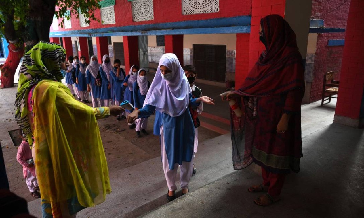 Um professoras verificam a temperatura e higienizam as mãos de alunas que chegam a escola em Lahore, no Paquistão Foto: ARIF ALI / AFP