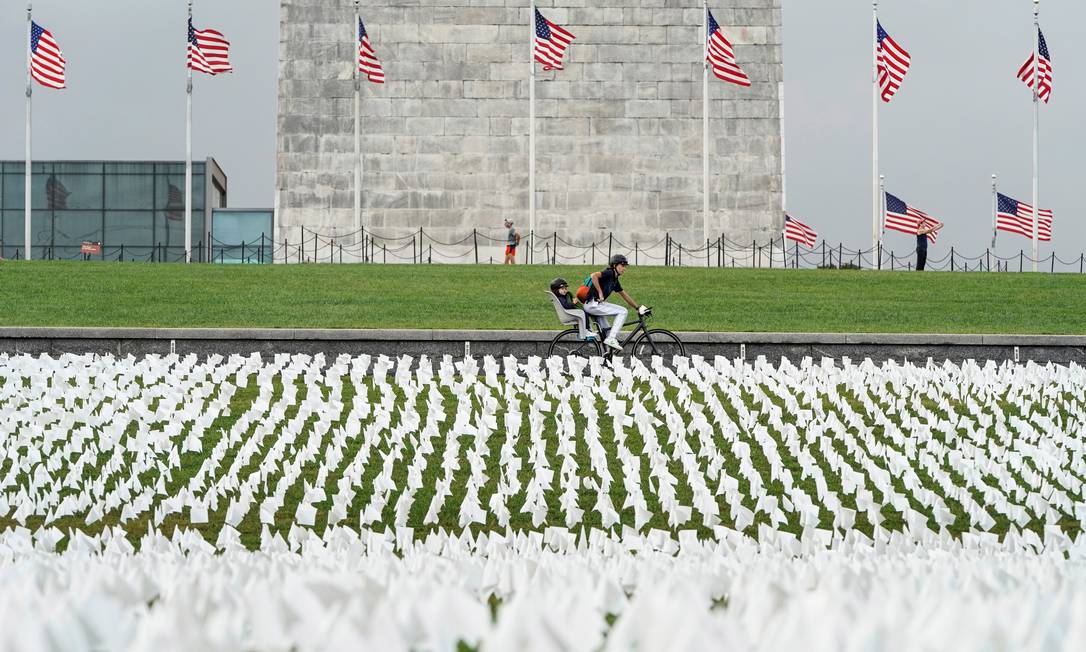 Ciclista pedala em frente a uma exposição de bandeiras brancas representando americanos que morreram de Covid-19, em Washington, EUA Foto: JOSHUA ROBERTS / REUTERS/17-09-2021