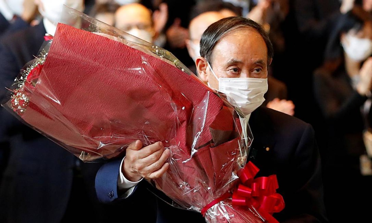 Yoshihide Suga, agora ex-primeiro-ministro do Japão, carrega buquê de flores ao deixar o gabinete, que passa a ser comandado por Fumio Kishida Foto: ISSEI KATO / REUTERS