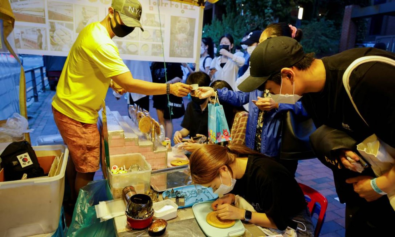 Nas ruas de Seoul, fãs da série tentam recortar o desenho no doce usando palito, sem quebrar a guloseima Foto: HEO RAN / REUTERS