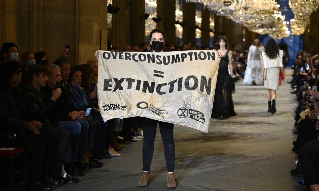 Ativista ambiental exibe um banner durante desfile da Paris Fashion Week, no Louvre, em Paris, para denunciar o impacto da indústria da moda nas mudanças climáticas Foto: CHRISTOPHE ARCHAMBAULT / AFP