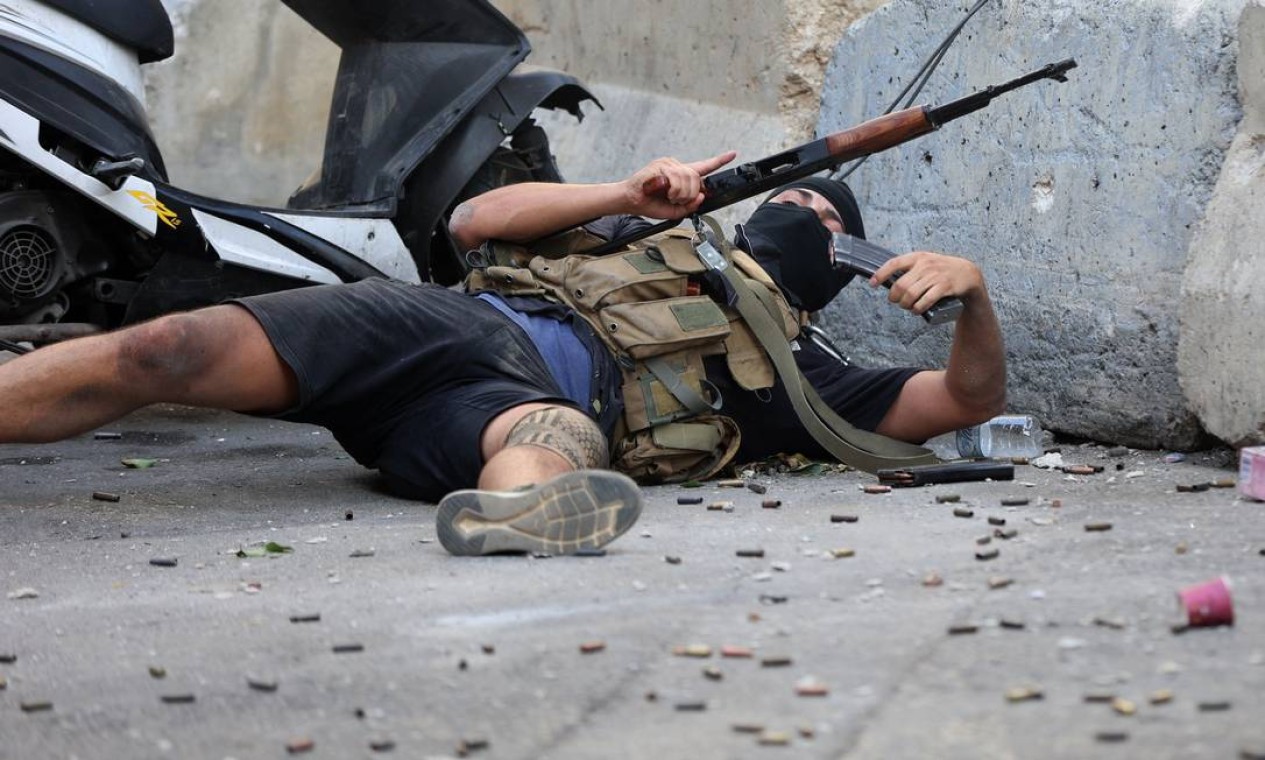 Abrigado em mureta de cimento, combatente do Hezbollah recarrega fuzil durante tiroteio Foto: ANWAR AMRO / AFP