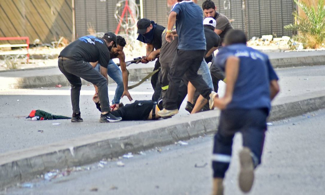 Membro da defesa civil corre para em direção a guerrilheiros que carregam corpo de homem morto durante confrontos Foto: - / AFP