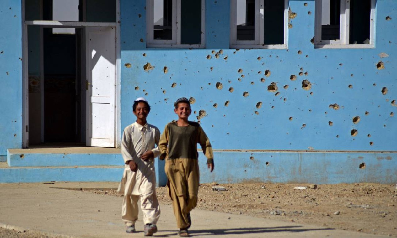 Crianças afegãs passam por sua escola repleta de marca de balas, na vila de Babro, no distrito de Arghandab Foto: JAVED TANVEER / AFP