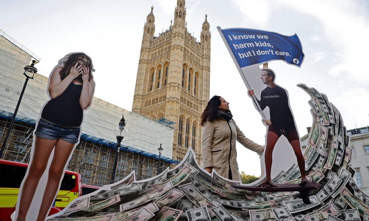 Instalação retrata o fundador do Facebook, Mark Zuckerberg, surfando em onda de dinheiro e cercado por adolescentes durante um protesto em frente ao Parlamento, no centro de Londres Foto: TOLGA AKMEN / AFP