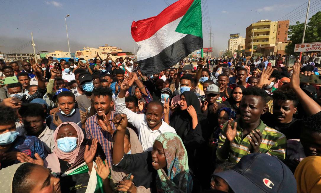 Manifestantes sudaneses erguem bandeiras nacionais enquanto se manifestam na capital Cartum, para denunciar as detenções noturnas de membros do governo Foto: - / AFP