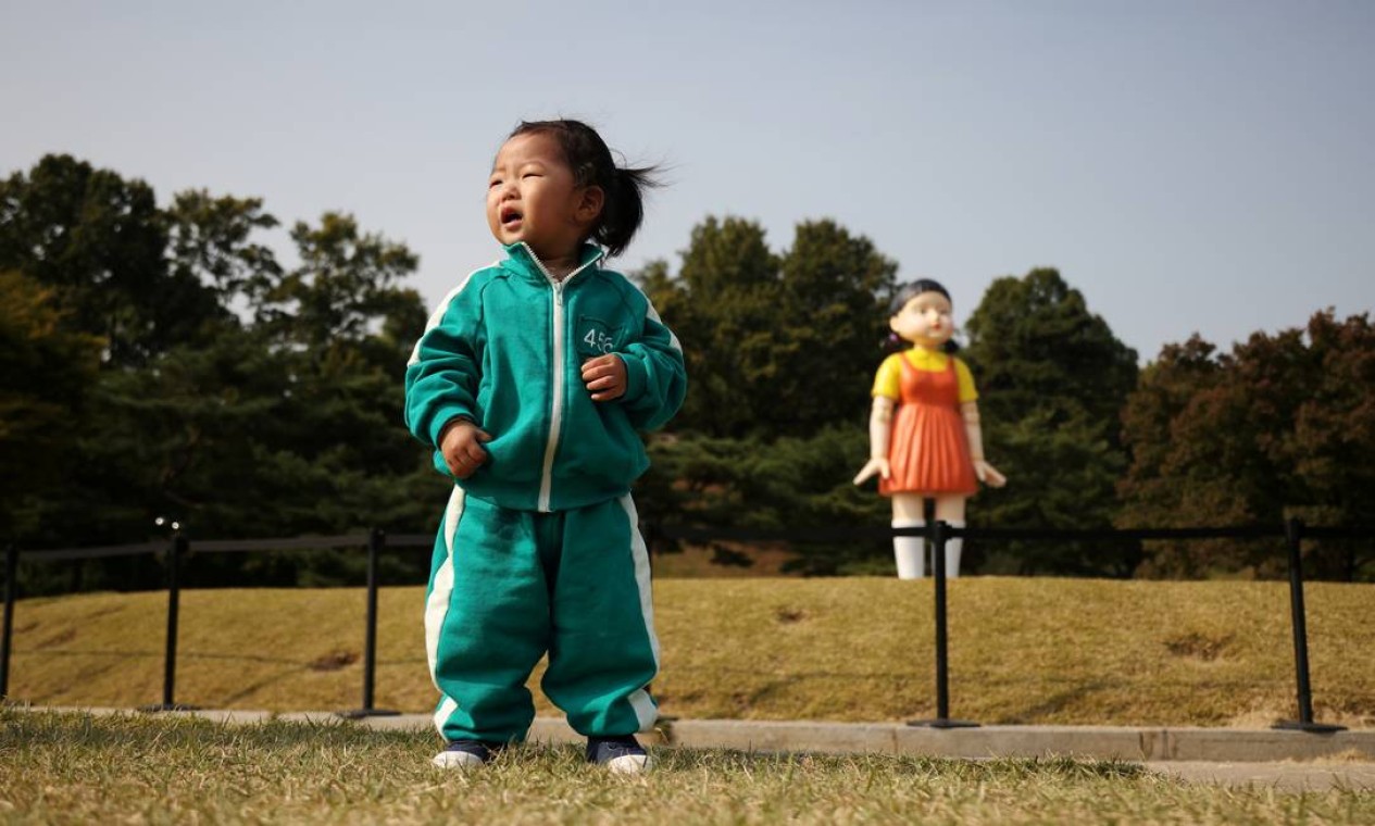 Criança vestindo fantasia da série 'Round 6' da Netflix posa para fotos em frente a uma boneca gigante chamada 'Younghee', em exibição em um parque em Seul, Coreia do Sul Foto: KIM HONG-JI / REUTERS