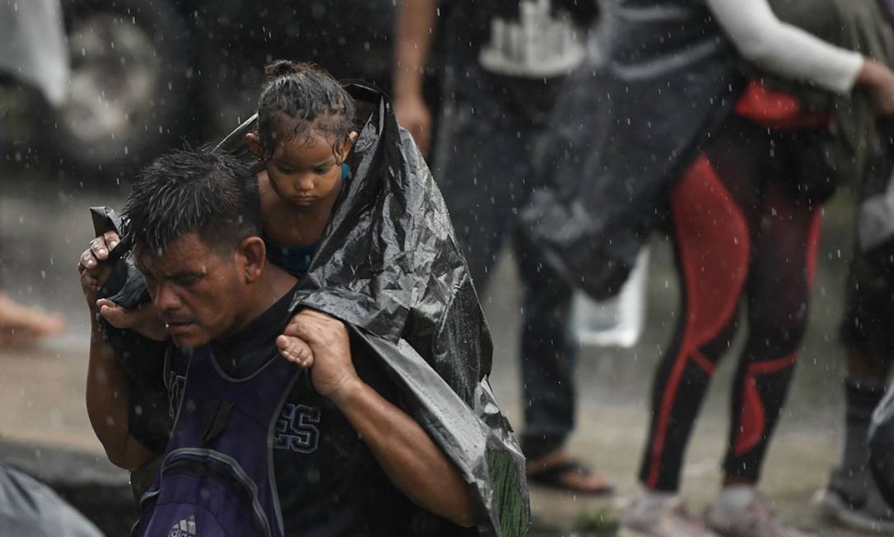 Migrante em uma caravana para os EUA carrega criança nos ombros sob a chuva em direção à Cidade do México para solicitar asilo e status de refugiado em Huixtla, Estado de Chiapas, México Foto: ISAAC GUZMAN / AFP