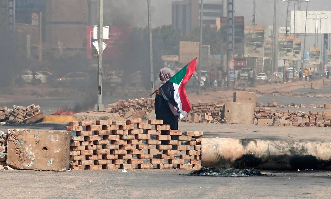 Manifestante sudanesa com uma bandeira nacional na capital Cartum um dia após militarem tomarem o poder do país Foto: AFP