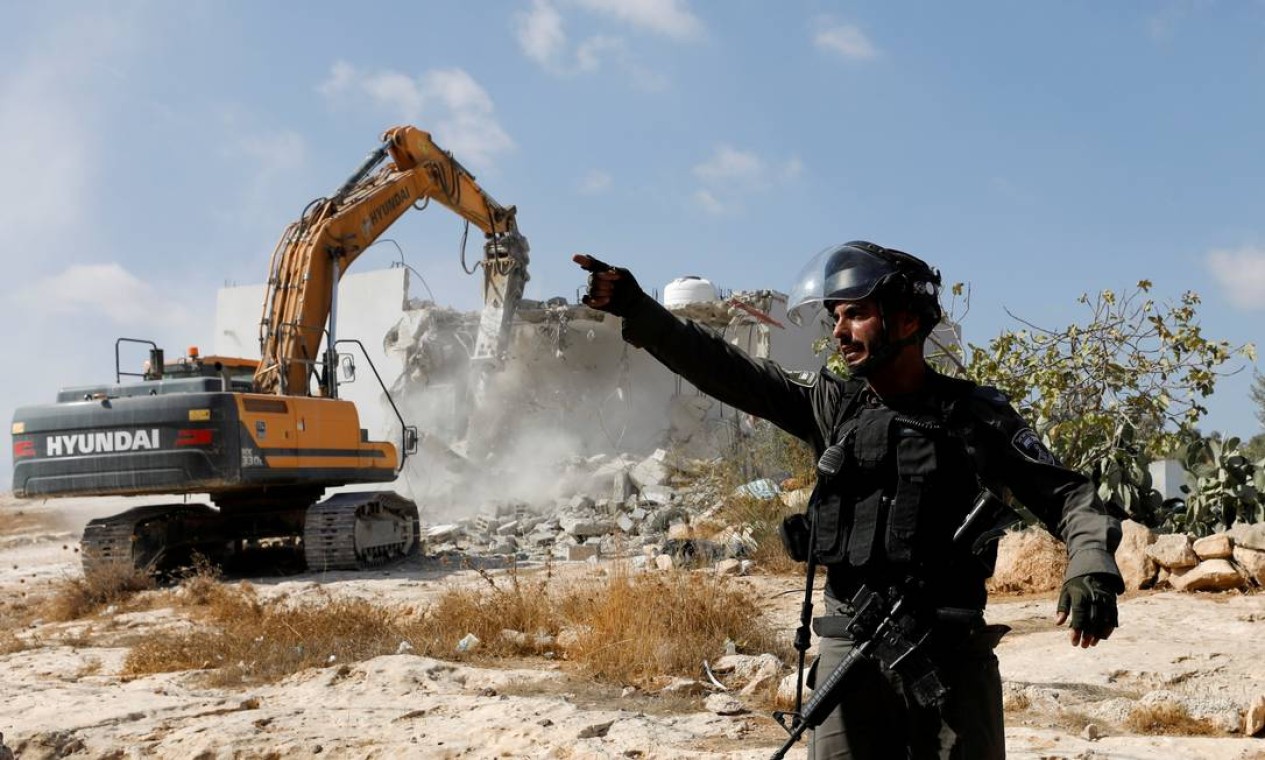 Um policial de fronteira israelense gesticula enquanto uma máquina destrói uma casa palestina perto de Yatta, na Cisjordânia ocupada por Israel Foto: MUSSA ISSA QAWASMA / REUTERS