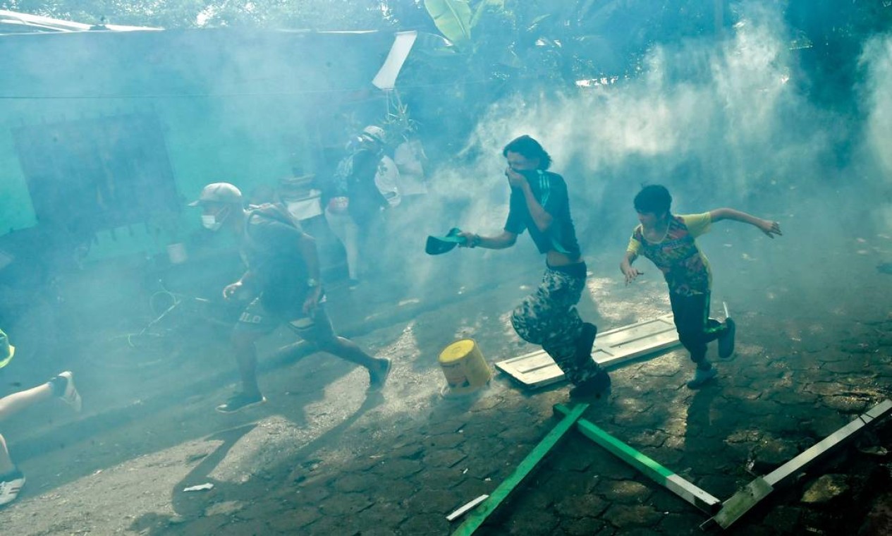 Pessoas fogem do gás lacrimogêneo disparado pela polícia de choque no bairro da Morávia enquanto as autoridades locais tentam implementar uma ordem de despejo para evacuar famílias que vivem em supostas construções ilegais, em Medellín, Colômbia Foto: JOAQUIN SARMIENTO / AFP