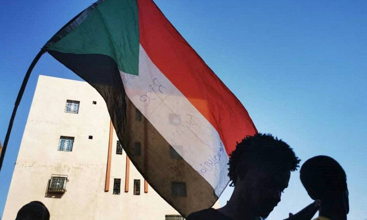 Jovens sudaneses agitam uma bandeira nacional enquanto protestam nas ruas da capital Cartum, contra o golpe militar Foto: - / AFP