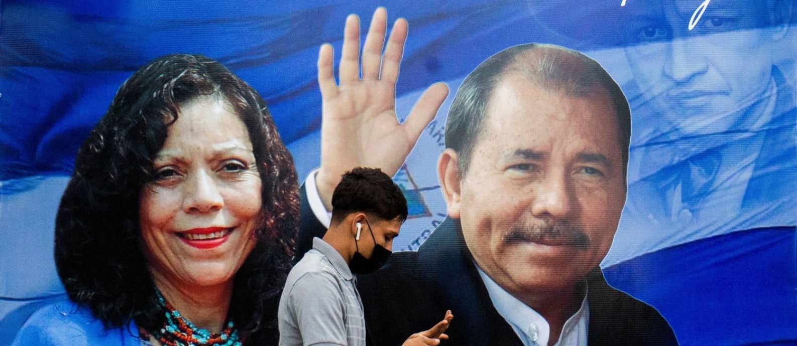 Homem checa telefone em frente a cartaz de Daniel Ortega e Rosario Murillo, sua mulher e vice-presidente; a abstenção eleitoral deve ser alta Foto: Maynor Valenzuela/ 25-9-2021 / Reuters