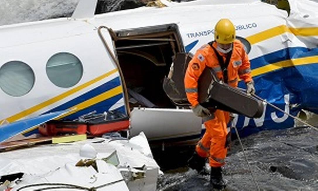 Integrante de equipe de resgate com estojo de violão em frente a avião onde estava Marília Mendonça Foto: Washingto Alves / Reuters
