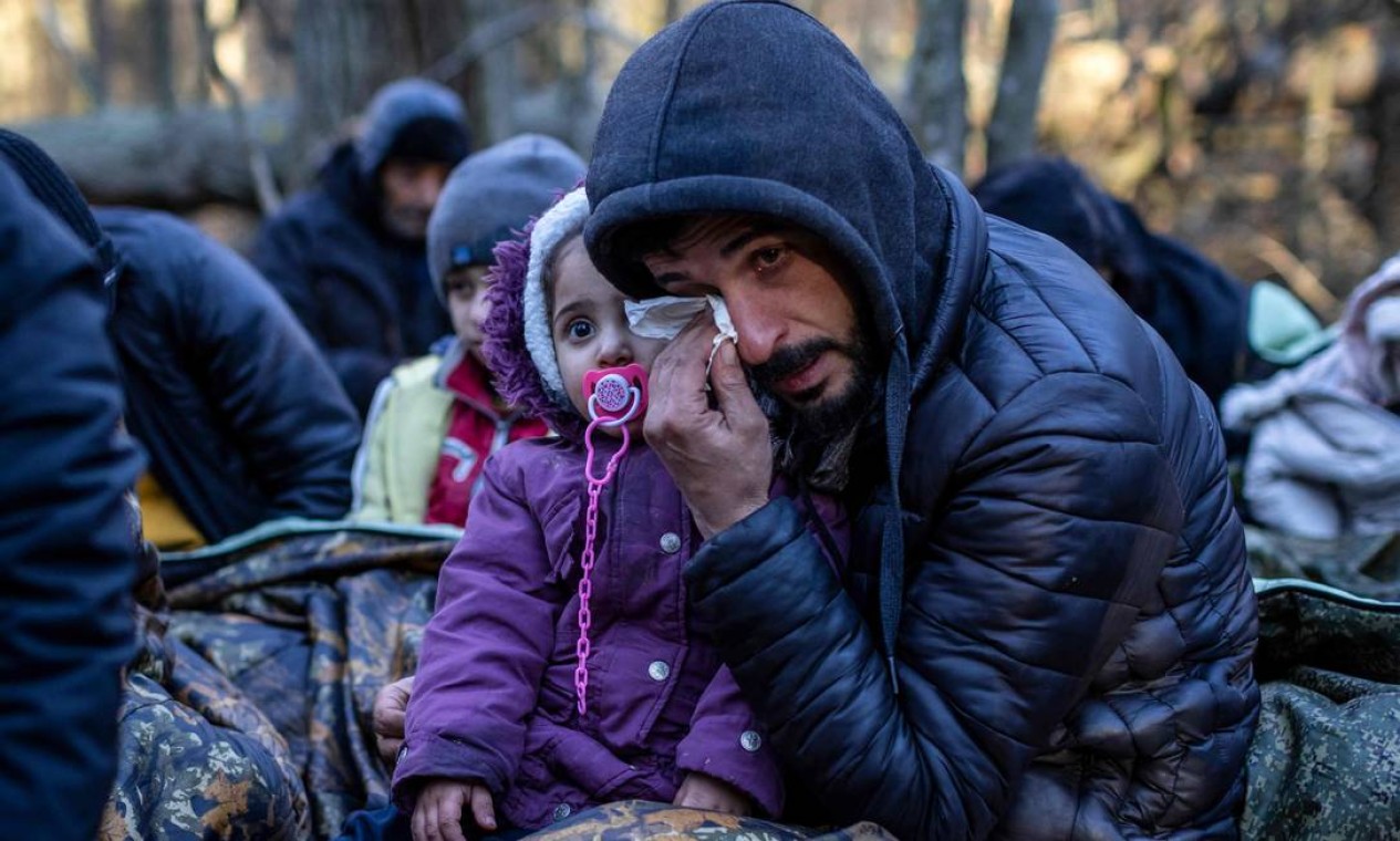 Homem curdo segurando uma criança chora enquanto esperam pela patrulha da guarda de fronteira, perto de Narewka, Polônia, perto da fronteira entre a Polônia e a Bielorrússia Foto: WOJTEK RADWANSKI / AFP