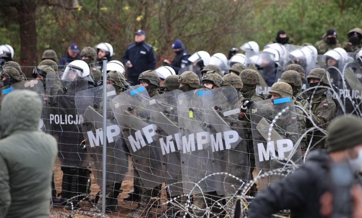 Policiais poloneses observando migrantes na fronteira entre a Bielorrússia e a Polônia Foto: LEONID SHCHEGLOV / AFP