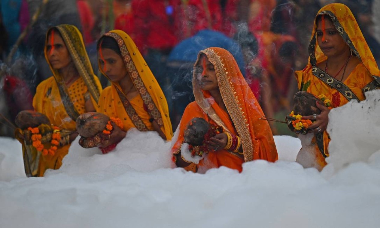 Devotos realizam rituais religiosos ao deus Sol em meio à espuma de poluição nas águas do rio Yamuna, na Índia Foto: MONEY SHARMA / AFP