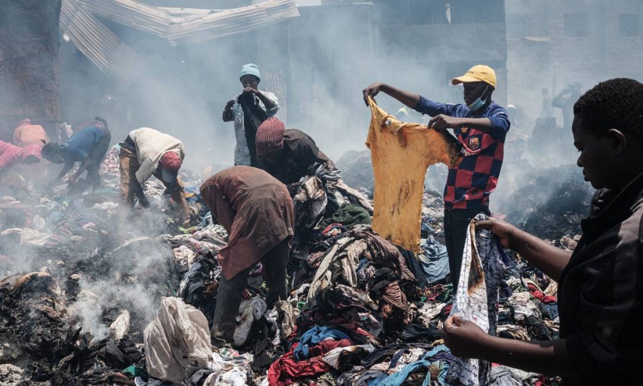 Comerciantes retiram roupas de entulhos queimados pelo fogo no mercado de Gikomba, o maior mercado de roupas de segunda mão da África Oriental, em Nairóbi, Quênia Foto: YASUYOSHI CHIBA / AFP